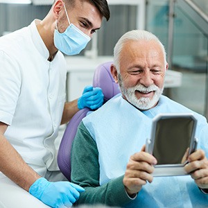 Man smiling at reflection in mirror with dental assistant