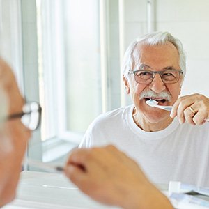 Man with glasses smiling while brushing his teeth