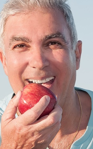 older man with implant dentures in Costa Mesa biting an apple