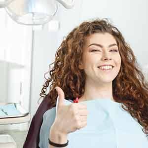 A red-headed woman giving a thumbs up in a dentist’s office