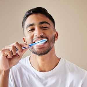 A young man brushing his teeth against a studio background