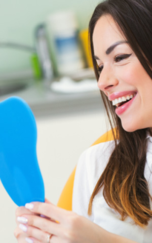 Woman admiring her smile in a mirror after teeth whitening in Costa Mesa
